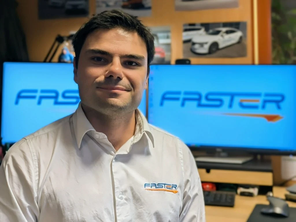 Person smiling and looking straight to the camera with cumpters on the background showing faster Racing logo